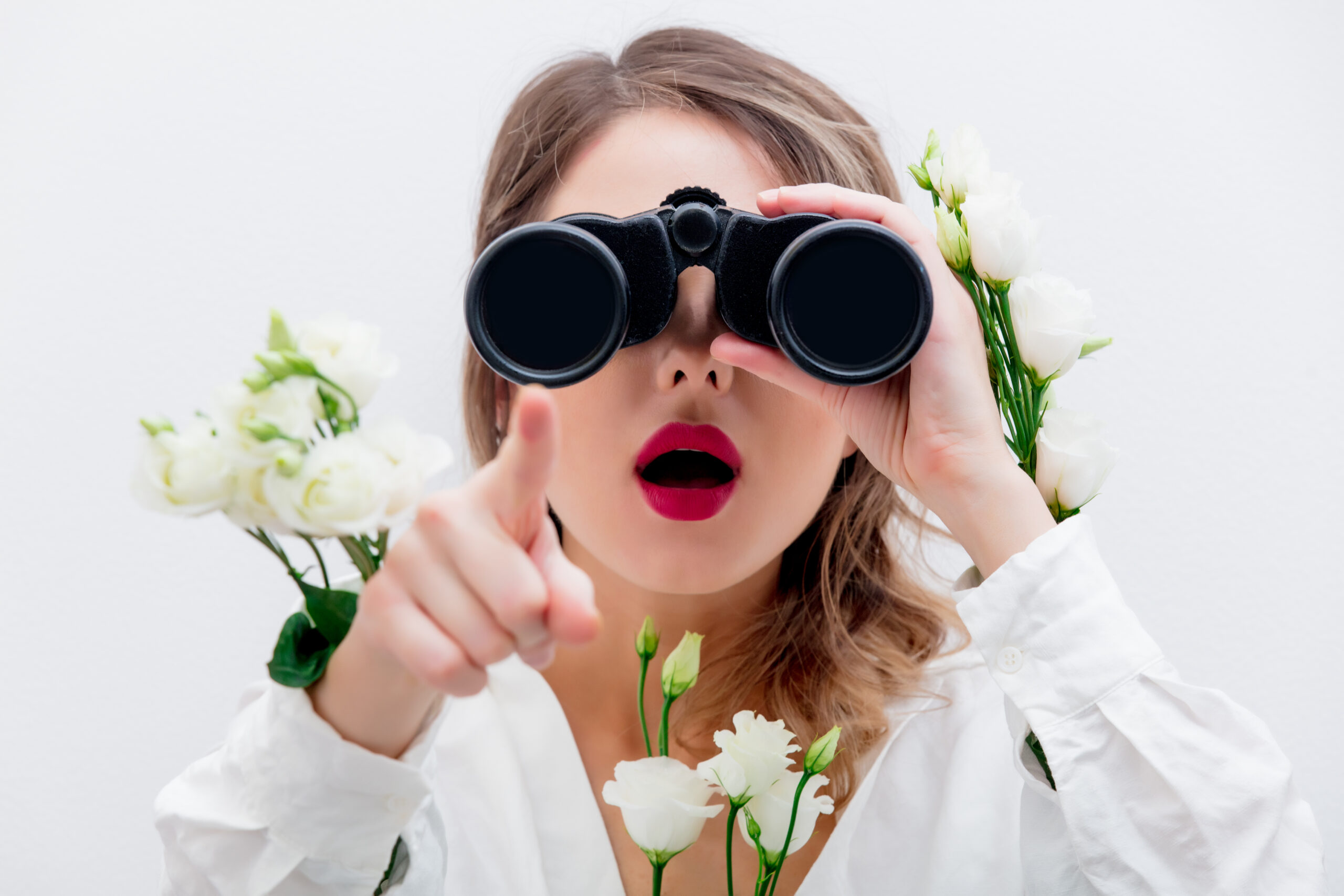 Beautiful woman with white roses in sleeves with binocular looking for something. Springtime concept or Valentines Day holiday